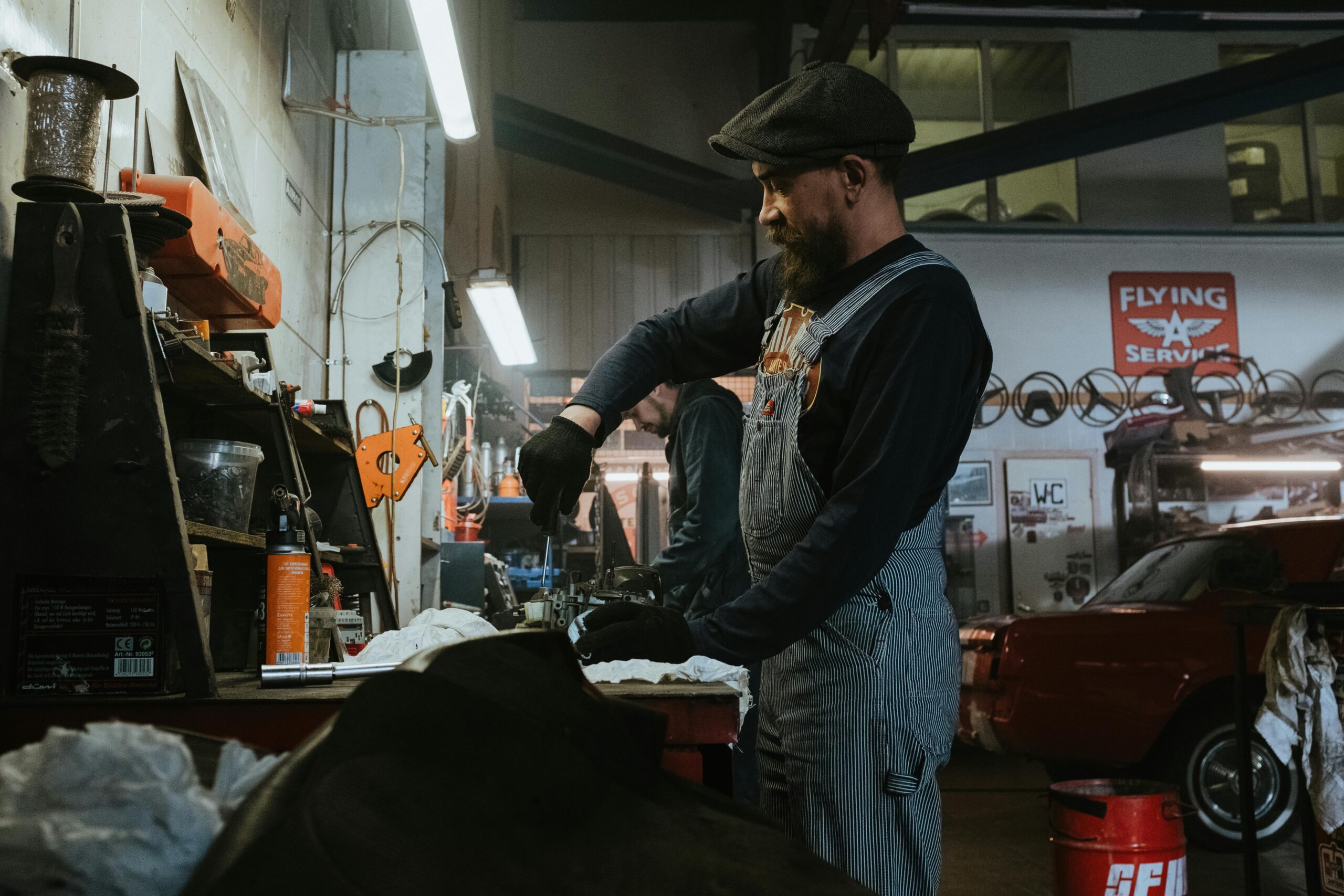 Mechanic performing repairs in a vintage garage setting, using tools and machinery.